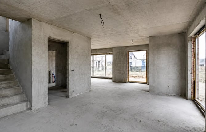 Afbouw van een casco woning met betonnen muren, ruw plafond en grote raampartijen als voorbereiding op strak stucwerk en verdere afwerking.