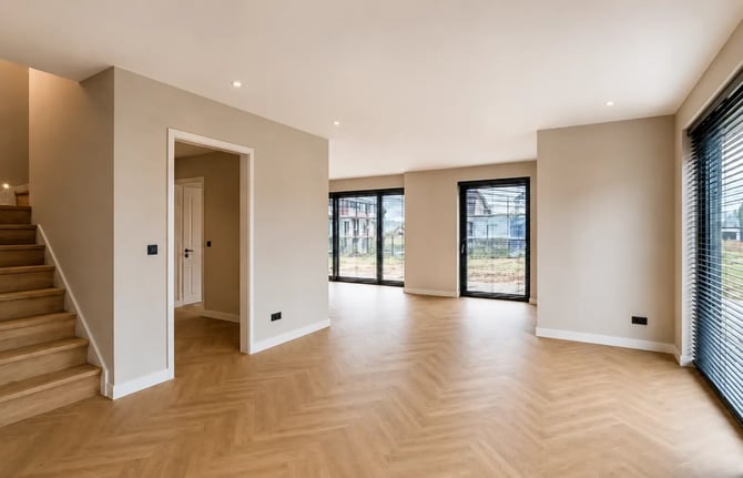 Afbouw van een woning met strak gestucte wanden, afgewerkt plafond, houten visgraatvloer en grote ramen voor een moderne woonruimte.