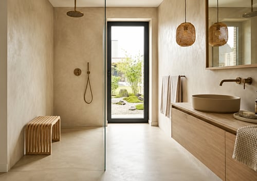 Betonstuc vloer in een moderne badkamer met natuurlijke uitstraling, houten wastafelmeubel, inloopdouche en warme beige wandafwerking.